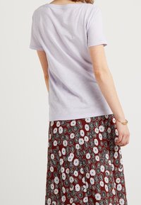 Ljuslila kortärmad t-shirt med rund halsringning, tillsammans med en bourgogne färgad kjol med blommönster som har svarta och vita blommor.