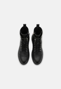 Bottines en cuir noir avec bout rond, lacets sur le devant, fermeture éclair sur le côté et accents texturés contrastants. Semelle plate avec peu de détails en matériel.