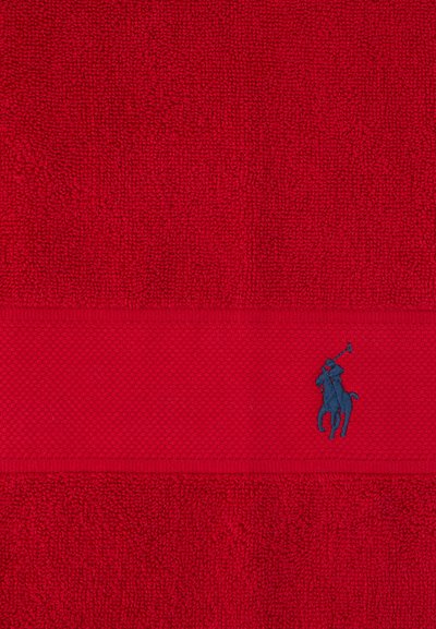 Rødt tekstureret stof med et vandret strikket bånd, der har en lille mørkeblå broderet polo-spiller på en hest.