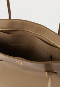 Barna bőr táska sima textúrával. Cipzáras rekesszel és logós címkével a belsejében. Hosszú fülek a hordozáshoz.