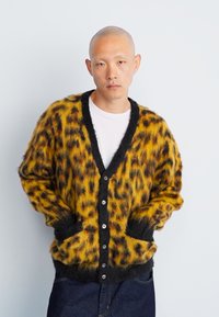 Κάρντιγκ με λεοπάρ σχέδιο σε κίτρινο και μαύρο, αφράτη υφή, μαύρες λεπτομέρειες και τσέπες. Διαθέτει κουμπιά μπροστά. Χαλαρή γραμμή.