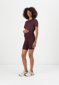Conjunto de roupa ativa de maternidade em bordeaux profundo, apresentando uma blusa de mangas curtas e calções de ciclismo ajustados, feitos de tecido elástico, combinados com ténis.