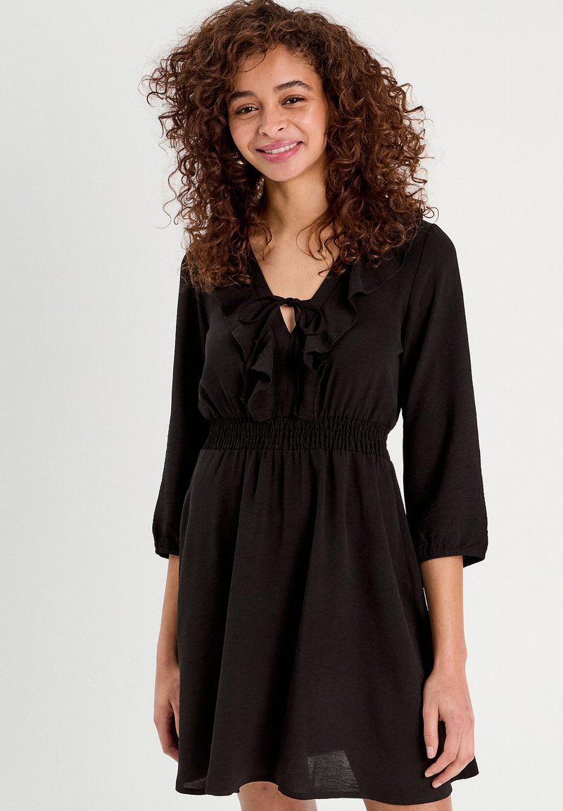 Robe noire avec un col froncé, des manches trois-quarts et une taille élastique. Tissu doux avec une silhouette fluide.