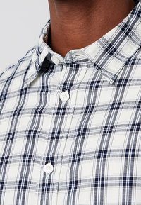 Geruit overhemd in wit, marineblauw en lichtblauw. Voorzien van een kraag met knopen, witte knopen en een katoenen textuur met horizontale en verticale strepen.