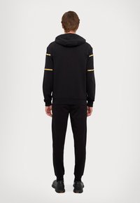 Black athletic outfit with a hoodie and pants. Features gold striped accents on the sleeves and a loose fit. Smooth texture, casual design.