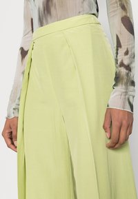 Calças largas verde-claro, com pregas na cintura. Textura suave, combinadas com uma blusa justa de mangas longas com padrão.
