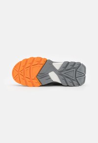 Semelle de chaussure de sport noire avec un motif en caoutchouc texturé. Des éléments de couleur orange et gris améliorent l'adhérence, avec une section centrale blanche.