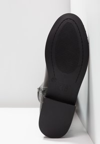 Suola di scarpa in pelle nera con fondo in gomma testurizzata a scanalature orizzontali, contrassegnata con la misura "37" e il nome del marchio "Xti".