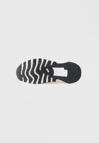 Suola di sneaker in gomma nera con motivo ondulato. Presenta un tallone rinforzato e scanalature laterali per la trazione, principalmente bianca con accenti neri.