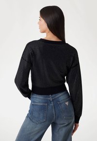 Must have black knit sweater with dotted texture, plain black cuffs, and hem. Paired with light blue denim jeans featuring back pockets and logo tag.