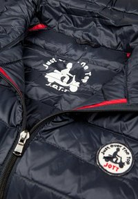 Mörkblå puffjacka med en röd detalj, en silverdragkedja och en grafisk logotyp i vitt med en person på en scooter inuti.