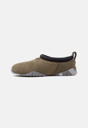 Lågstansad casual slip-on-sko i olivgrönt mocka med svart vadderad krage och grå texturerad gummisula, sidovy.