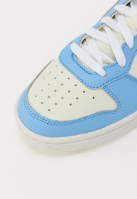 Baskets bleu clair et crème avec des perforations, des lacets blancs et une texture en cuir lisse avec des détails de couture contrastés.