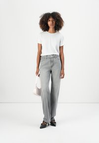 Grå vide jeans med belte, sammen med en kortermet hvit t-skjorte. Holder en lys rosa håndveske. Svarte spisse sko.