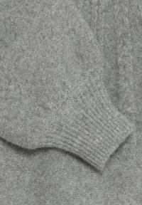 Dettaglio di un maglione grigio lavorato a maglia che mostra il polsino a costine, la morbidezza della trama e la superficie liscia con un motivo sottile in tutto il capo.