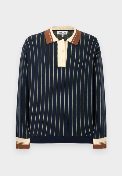 Πλεκτό μπλε ναυτικό πόλο πουλόβερ με κάθετες ανοιχτό κίτρινες ρίγες. Διαθέτει μπεζ πατιλέτα με τρία κουμπιά και αντίθετο καφέ γιακά και μανσέτες.