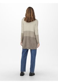 Lungo maglione a maglia a strisce beige e taupe, con vestibilità ampia e spalle basse. Abbinato a jeans a gamba larga blu e scarpe nere.