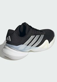 Μαύρα αθλητικά παπούτσια με υφασμένο αεριζόμενο επάνω μέρος, ασημί ρίγες και επένδυση για απορρόφηση κραδασμών στο λευκό πάτο. Η πίσω πλευρά διαθέτει στρογγυλεμένη σχεδίαση στη φτέρνα.