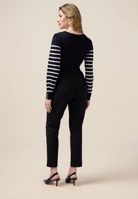 Marinblå och vit randig långärmad topp med knappdetaljer, kombinerad med svarta tapered-byxor och svarta slingback-klackar. Slät textur.
