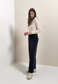 Roomkleurige, gebreide top met lange mouwen gecombineerd met een donkerblauwe, hooggehate broek en witte sneakers met lichtgrijze accenten. Simpel, op maat gemaakt ontwerp.