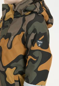 Camo-jakke i grønne, brune og sennepsfarvede nuancer. Har hætte og broderet logo på ærmet. Materialet er glat og holdbart.