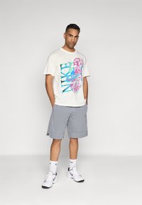 Kerasa kaos krim dengan reka bentuk grafik berwarna-warni yang menampilkan "NIKE"; dipadankan dengan seluar pendek kelabu muda dan kasut sukan putih. Komposisi yang sederhana.