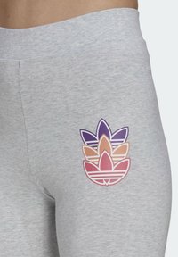 Tätt in på ljusgrå leggings med en tredubbel lager Adidas trefoil-logotyp i lila, persika och rosa på övre låret.