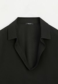 Chemise noire à col avec manches longues et ouverture en V, avec une étiquette "Massimo Dutti" à l'intérieur de l'encolure.