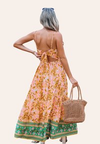 Vestido maxi amarillo con estampados florales en rosa y azul, cierre en la parte de atrás, detalle recortado y borde floral verde. Bolsa de mimbre tejida en mano.