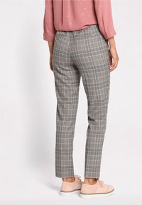 Pantalons à carreaux gris avec une coupe ajustée, présentant des accents noirs et roses, associés à des chaussures rose clair et un blouse rose.