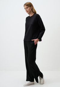 Czarna bluzka z długim rękawem o luźnym kroju, zestawiona z czarnymi spodniami o szerokich nogawkach. Białe sneakersy mają strukturalny wzór i zapięcie na sznurówki.