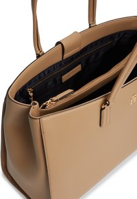 Μπεζ δερμάτινη τσάντα χειρός με δύο λουριά, ανοιχτή για να αποκαλύπτεται η εσωτερική επένδυση από μαύρο ύφασμα και πολλαπλές θήκες με φερμουάρ.