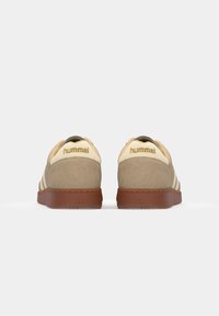 Beige and cream suede sneakers with three white side stripes, brown rubber soles, and embossed branding on the heel tab.