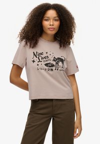 Lyserød cropped t-shirt i bomuld med sort grafisk tryk af en kat og vinyl, med stjerner og japansk tekst. Korte ærmer og rund hals.