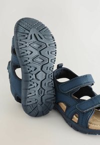 Mörkblå sandaler med justerbara remmar, texturerade gummisulor och en vadderad innersula. Öppen design med utskärningar för andningsförmåga.