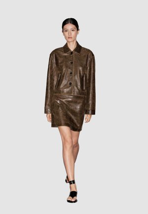Brown leather jacket dress with a collar, long sleeves, and front buttons; features side pockets and a smooth texture. Black footwear.