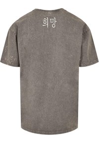 Camiseta gris de gran tamaño hecha de algodón, con un cuello redondo ribeteado y texto en coreano "희망" impreso en la parte posterior. Tejido suave y texturizado.