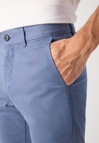 Pantalon en coton bleu clair avec une coupe slim, poches latérales et fermeture à bouton. Texture lisse avec des détails de couture subtils.