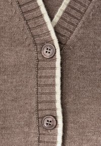 Cárdigan marrón con acentos crema, diseño de escote en V, puños acanalados y un botón redondo oscuro con cuatro agujeros. Tejido de punto suave y texturizado.
