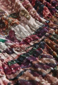 Gros plan d'un tissu multicolore avec des motifs en relief texturés et des zones froncées, plissées, dans des nuances de rouge, vert, marron, noir et blanc.