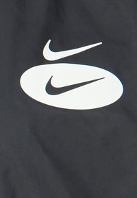 Zwarte stof met een groot wit Nike-logo met gestileerde swooshes. Het ontwerp is strak met gladde randen en een contrasterend kleurenpalet.