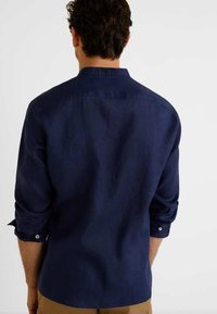 Marineblauw linnen overhemd met een kraag, lange opgerolde mouwen en knoopdetails. Soepele textuur zonder patronen, casual ontwerp.