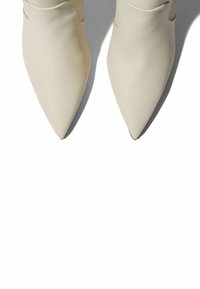 Botas de tobillo de punta afilada de color crema, hechas de cuero suave, con un diseño minimalista y sutiles detalles de costura.