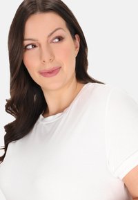 Hvid t-shirt med korte ærmer og rund halsudskæring, glat tekstur og afslappet pasform, båret af en model med langt mørkt hår.