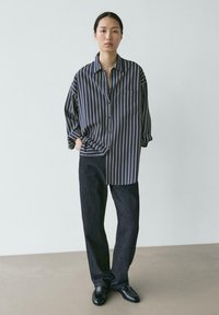 Marineblau gestreiftes Hemd mit Knopfleiste und Tasche, lockere Passform, kombiniert mit dunklen Denim-Hosen mit geradem Bein und schwarzen Slippern. Minimalistisches Design.