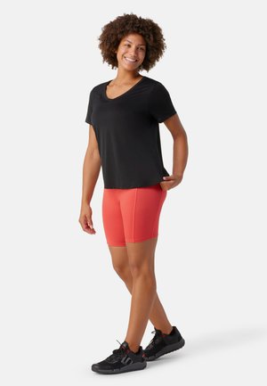 Maglietta nera a maniche corte con scollo a V abbinata a pantaloni sportivi corallo luminosi e sneaker nere. Il tessuto sembra leggero e elasticizzato.
