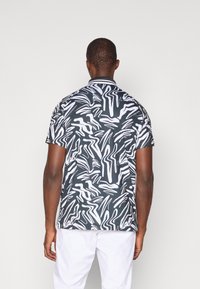 Camisa de manga curta com um padrão abstrato em preto e branco. O tecido parece leve, com uma textura suave e um colarinho.