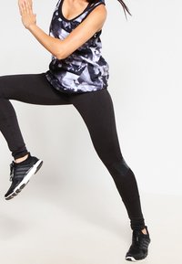 Leggings neri sportivi e una canotta a fantasia realizzata in tessuto leggero. La canotta presenta un design grafico in tonalità di nero e grigio.