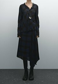 Schwarz und navy-blau kariertes Blusenshirt mit fransigen Kanten, kombiniert mit einem passenden asymmetrischen Rock. Getragen mit knielangen schwarzen Stiefeln und einer Pendel-Halskette.