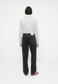 Grijze langemouwen shirt met ronde hals, gedragen met zwarte losse spijkerbroek en roodgestreepte schoenen, gezien vanuit de achterkant.